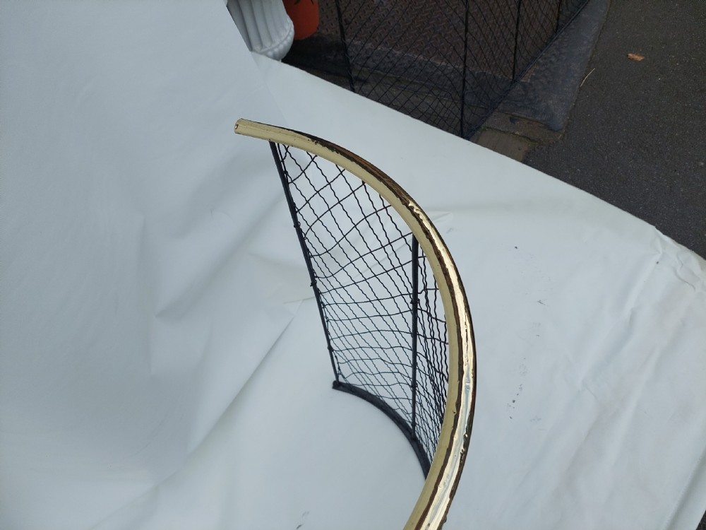 A tall, curved Victorian nursery fender constructed from black wire mesh with vertical iron supports and a polished brass top rail. View V