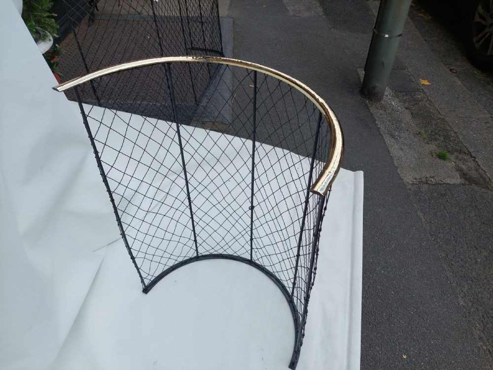 A tall, curved Victorian nursery fender constructed from black wire mesh with vertical iron supports and a polished brass top rail. View VI