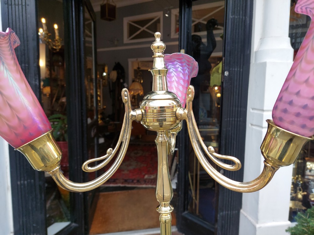 An early 20th-century Art Nouveau polished brass adjustable standard lamp featuring a tripod base with whiplash curves and three arms holding pink fluted glass shades. View VI