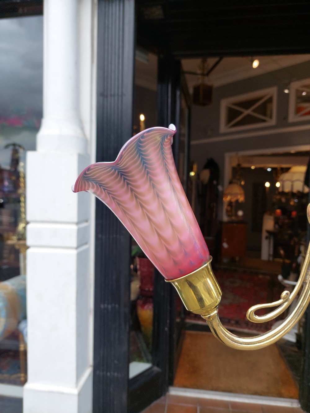 An early 20th-century Art Nouveau polished brass adjustable standard lamp featuring a tripod base with whiplash curves and three arms holding pink fluted glass shades. View IX