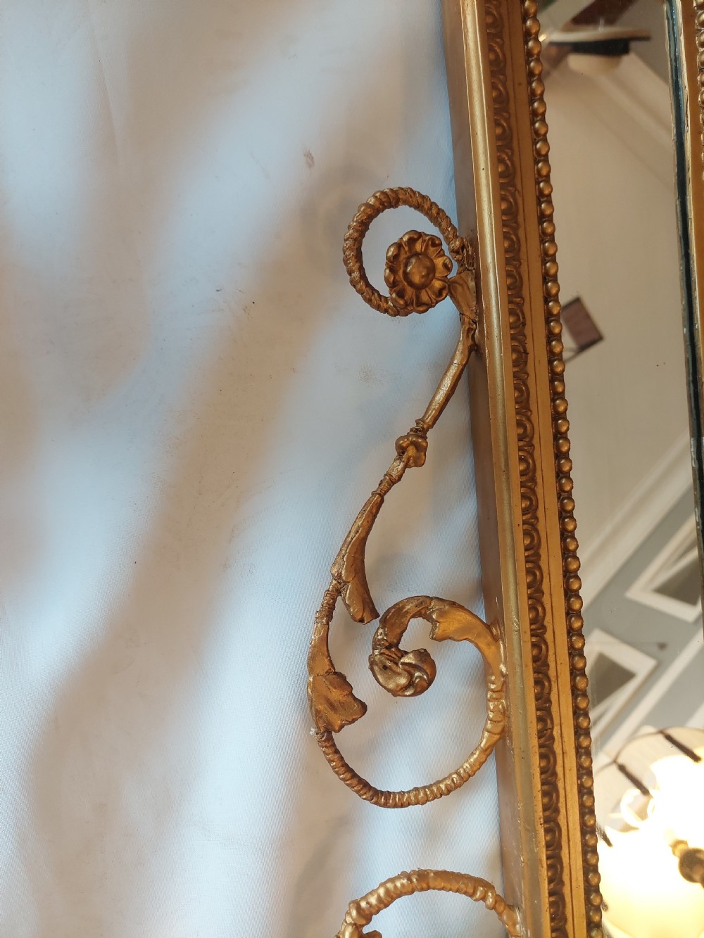 A late 19th-century Adam Revival gilt-gesso wall mirror featuring an urn and garland cresting, beaded frame moulding, and bevelled mirror plates. View III