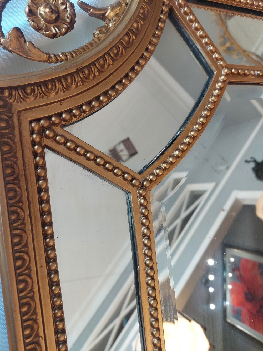 A late 19th-century Adam Revival gilt-gesso wall mirror featuring an urn and garland cresting, beaded frame moulding, and bevelled mirror plates. View IV