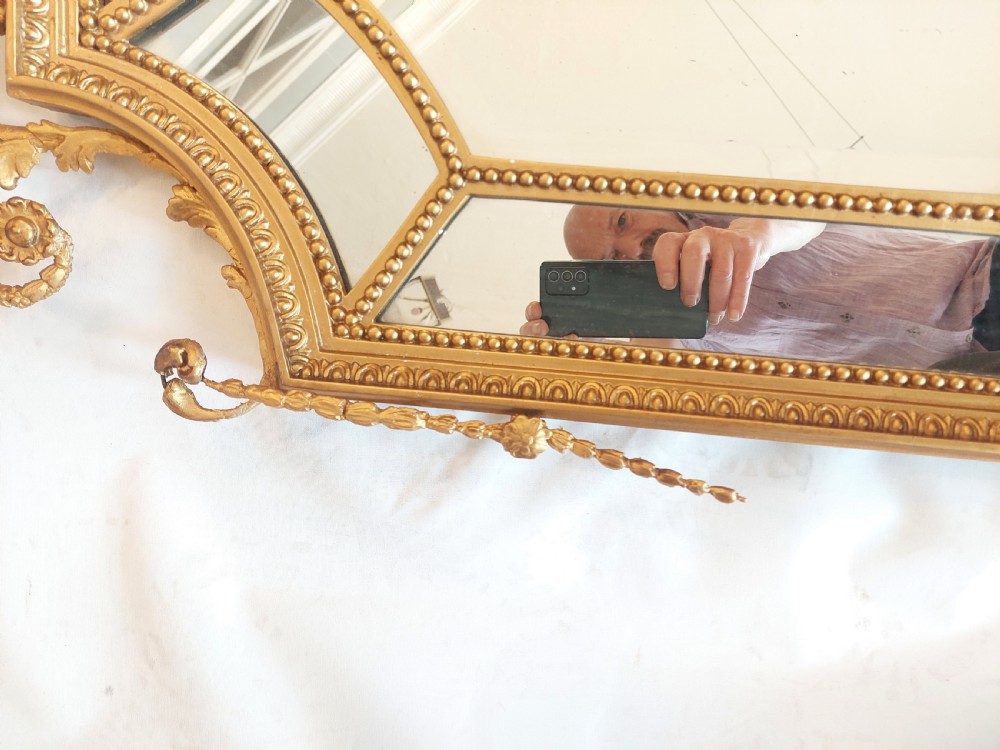 A late 19th-century Adam Revival gilt-gesso wall mirror featuring an urn and garland cresting, beaded frame moulding, and bevelled mirror plates. View V