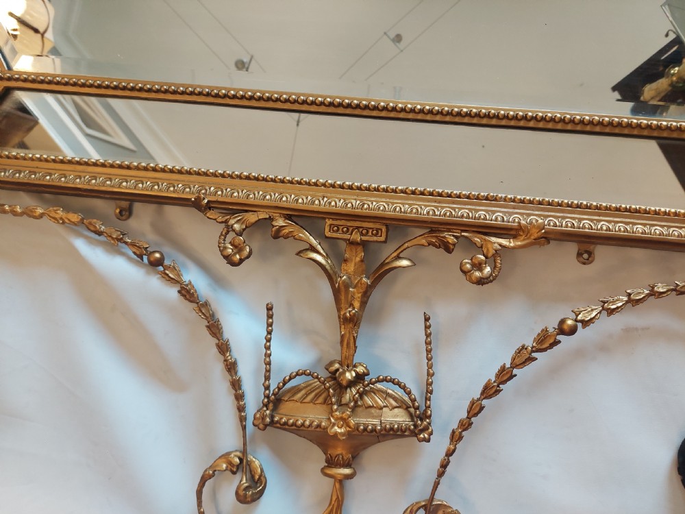 A late 19th-century Adam Revival gilt-gesso wall mirror featuring an urn and garland cresting, beaded frame moulding, and bevelled mirror plates. View VII