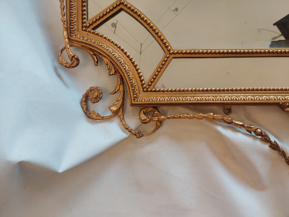 A late 19th-century Adam Revival gilt-gesso wall mirror featuring an urn and garland cresting, beaded frame moulding, and bevelled mirror plates. View VIII