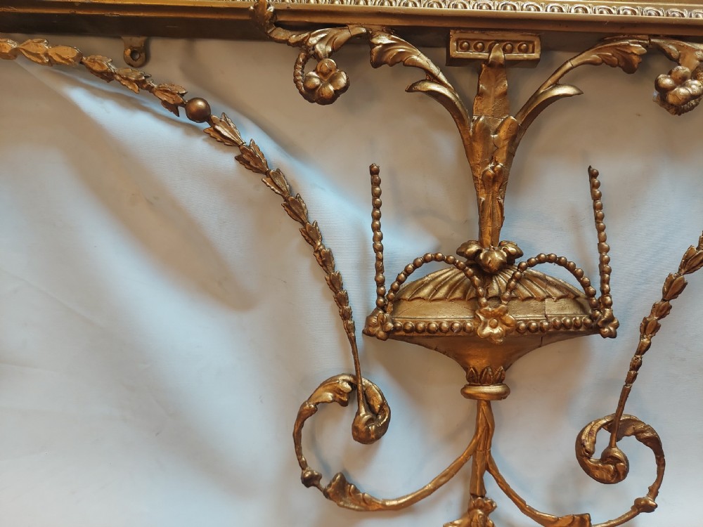 A late 19th-century Adam Revival gilt-gesso wall mirror featuring an urn and garland cresting, beaded frame moulding, and bevelled mirror plates. View IX