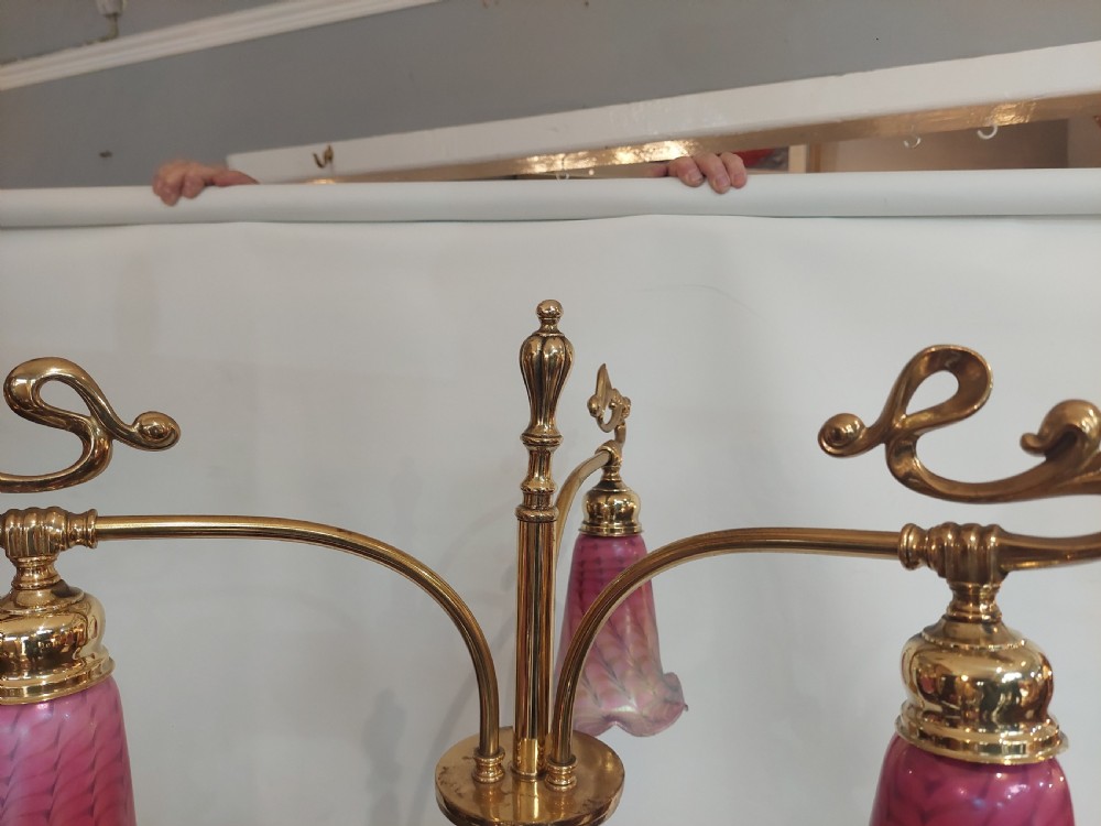 An Art Nouveau brass standard lamp with a slender central column, three curving arms holding frilled pink glass shades, and a tripod base. View IV