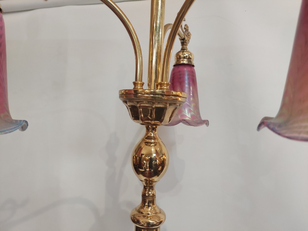 An Art Nouveau brass standard lamp with a slender central column, three curving arms holding frilled pink glass shades, and a tripod base. View V