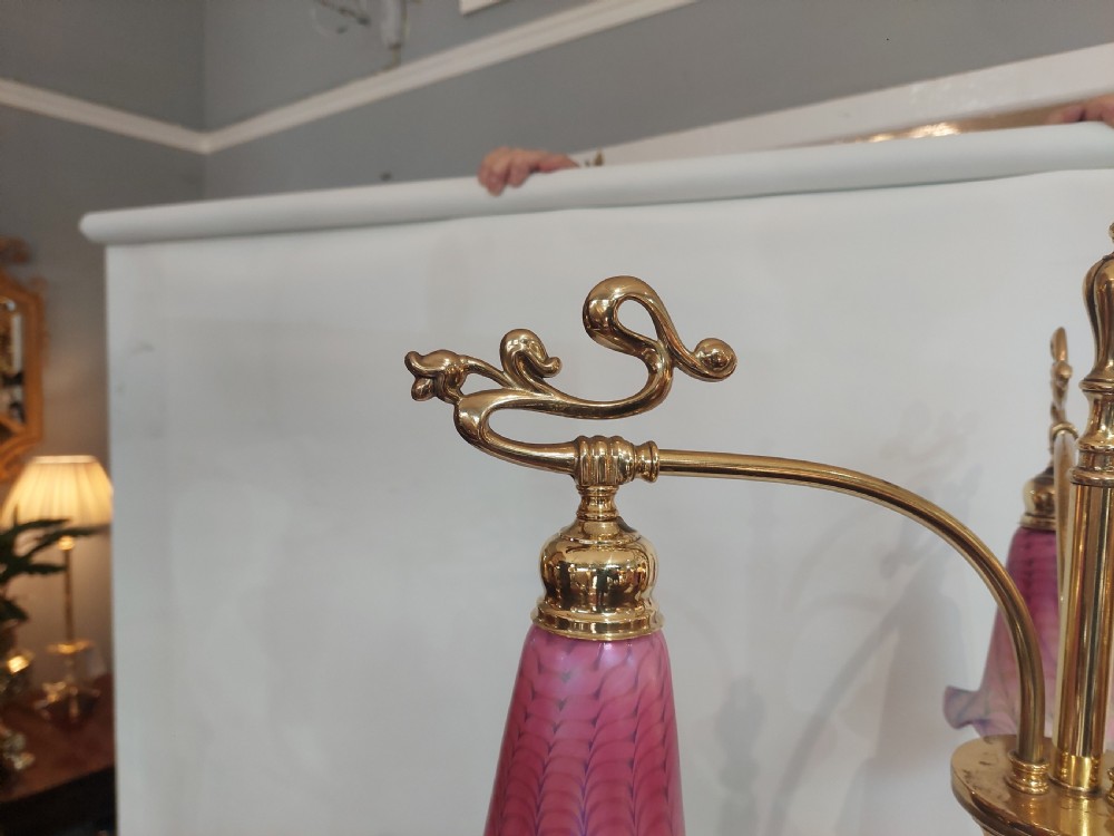 An Art Nouveau brass standard lamp with a slender central column, three curving arms holding frilled pink glass shades, and a tripod base. View VI