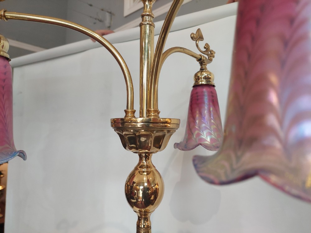 An Art Nouveau brass standard lamp with a slender central column, three curving arms holding frilled pink glass shades, and a tripod base. View VII