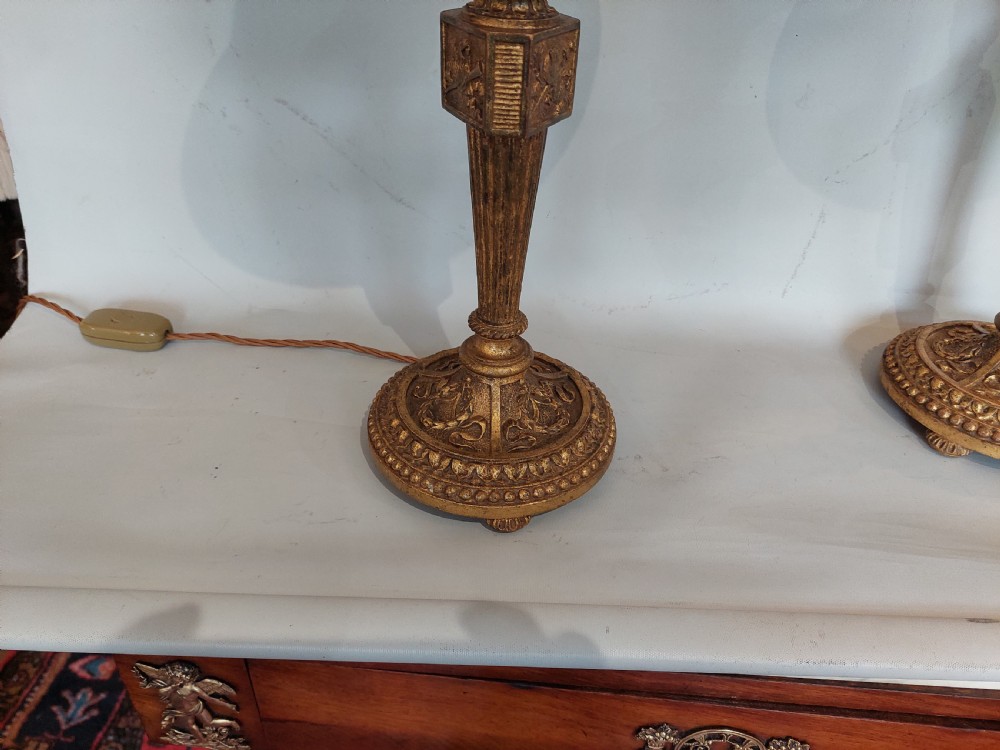 A pair of early 19th-century French giltwood candlestick table lamps with fluted columns, square relief blocks, circular beaded bases, and cream flared shades. View III