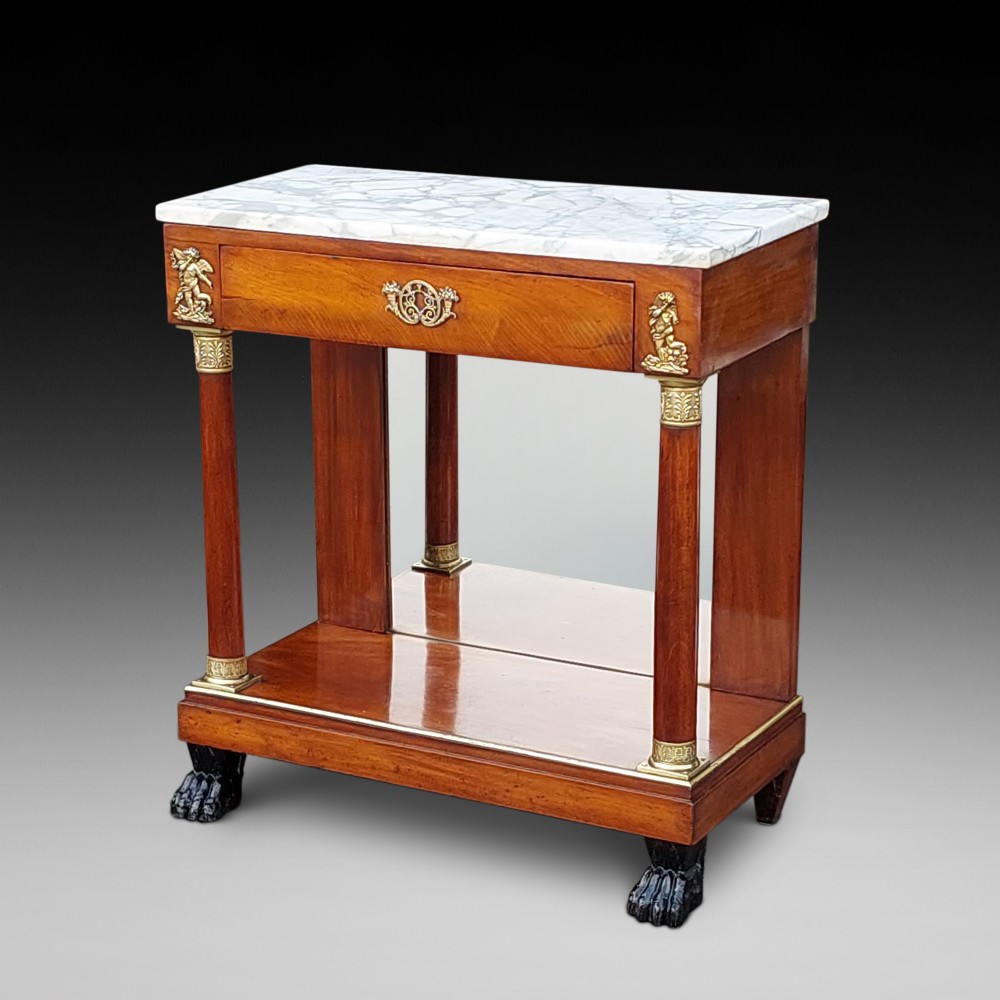 An early twentieth-century French Empire style console table crafted from mahogany with a grey-veined white marble top, columnar legs with gilt mounts, a mirrored back, and carved paw feet.