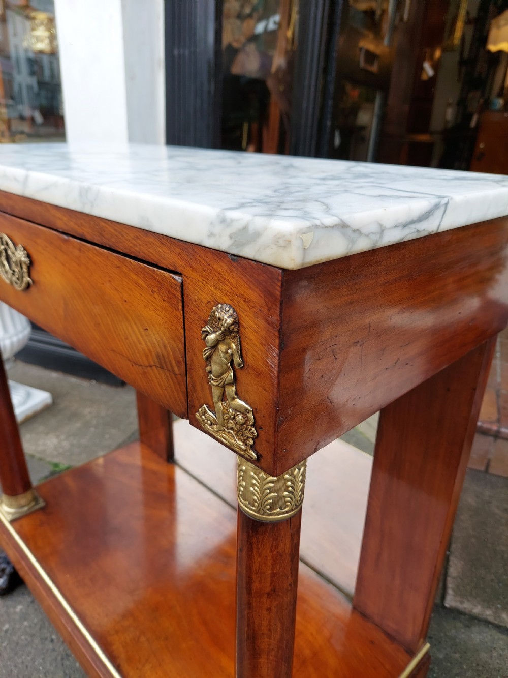 An early twentieth-century French Empire style console table crafted from mahogany with a grey-veined white marble top, columnar legs with gilt mounts, a mirrored back, and carved paw feet. View III