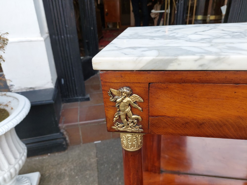 An early twentieth-century French Empire style console table crafted from mahogany with a grey-veined white marble top, columnar legs with gilt mounts, a mirrored back, and carved paw feet. View V