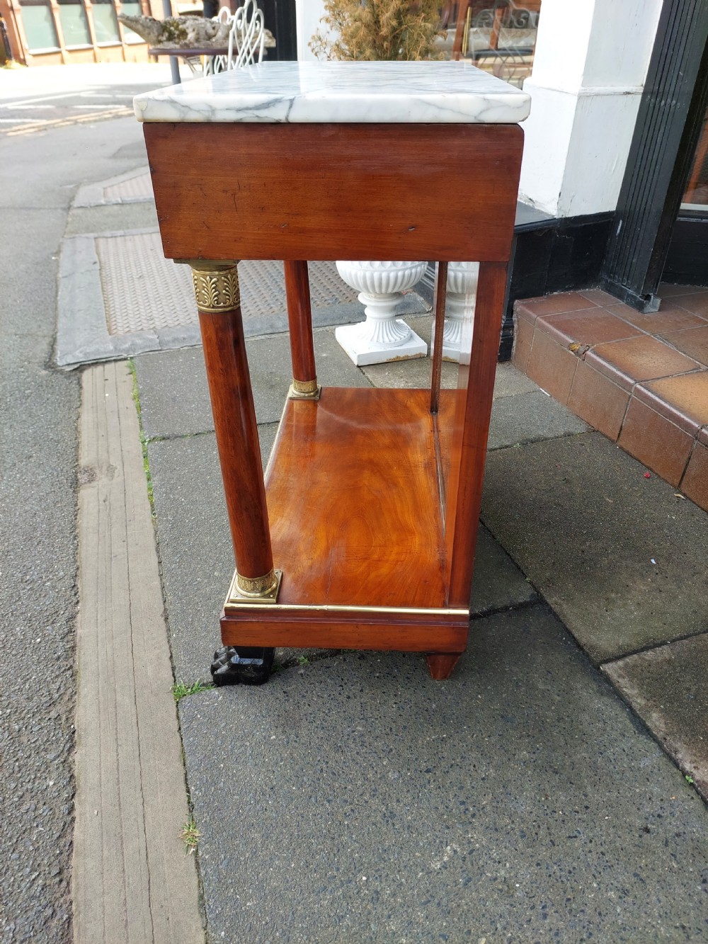 An early twentieth-century French Empire style console table crafted from mahogany with a grey-veined white marble top, columnar legs with gilt mounts, a mirrored back, and carved paw feet. View VIII