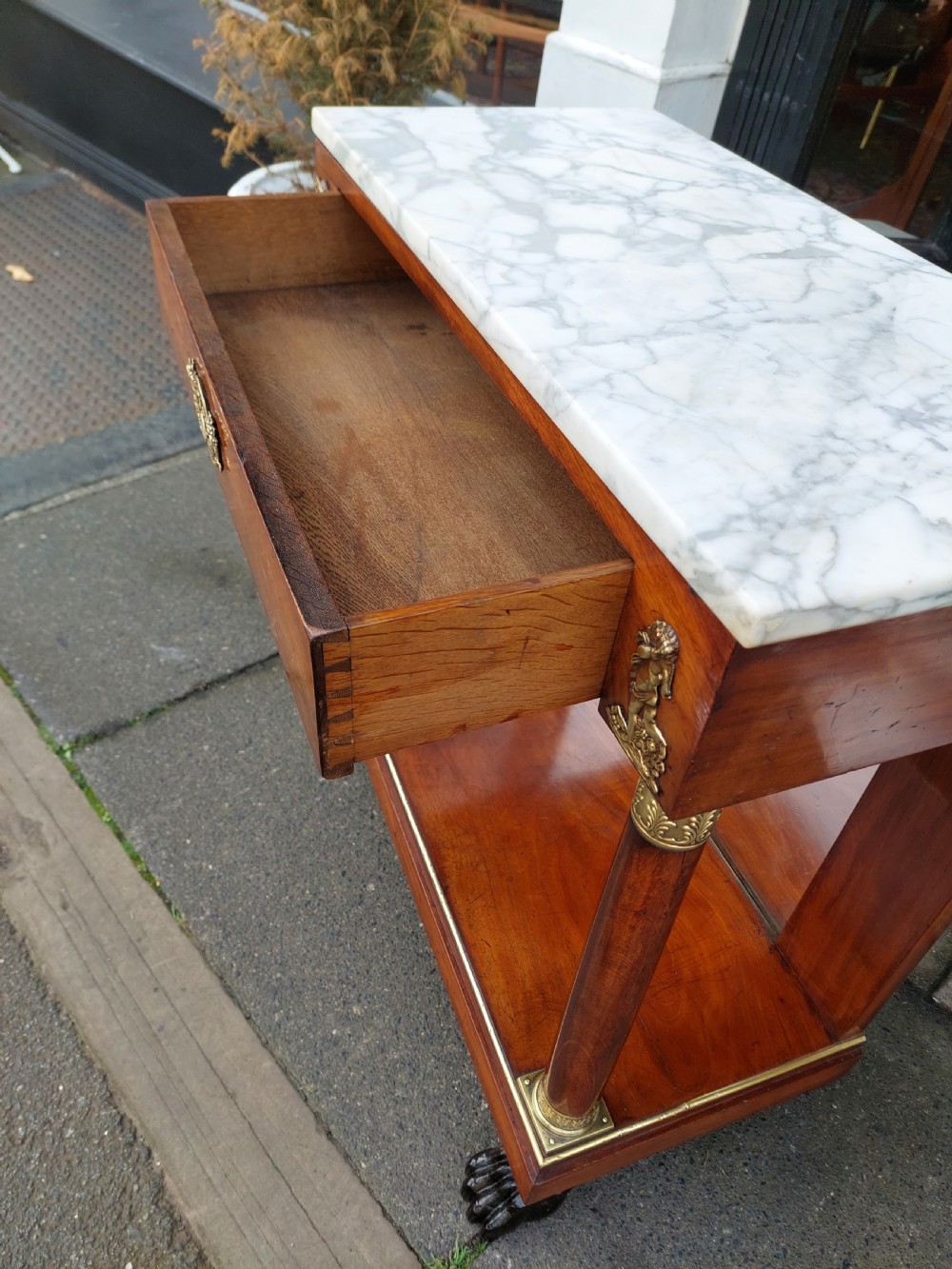 An early twentieth-century French Empire style console table crafted from mahogany with a grey-veined white marble top, columnar legs with gilt mounts, a mirrored back, and carved paw feet. View IX