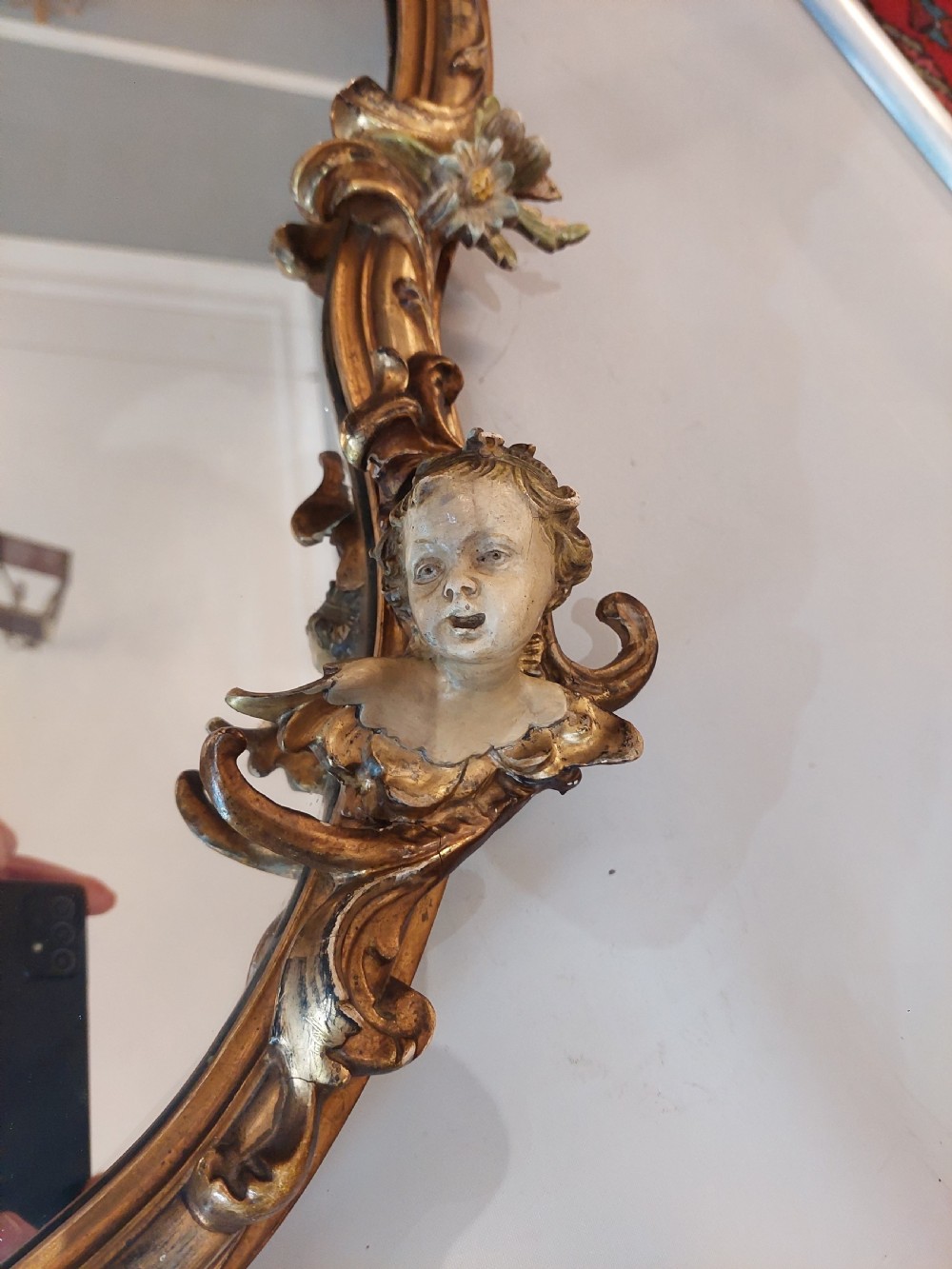 An early 20th-century Italianate giltwood wall mirror featuring an intricate carved crest, asymmetric Rococo scrolls, floral accents, and sculpted putti heads. View IV
