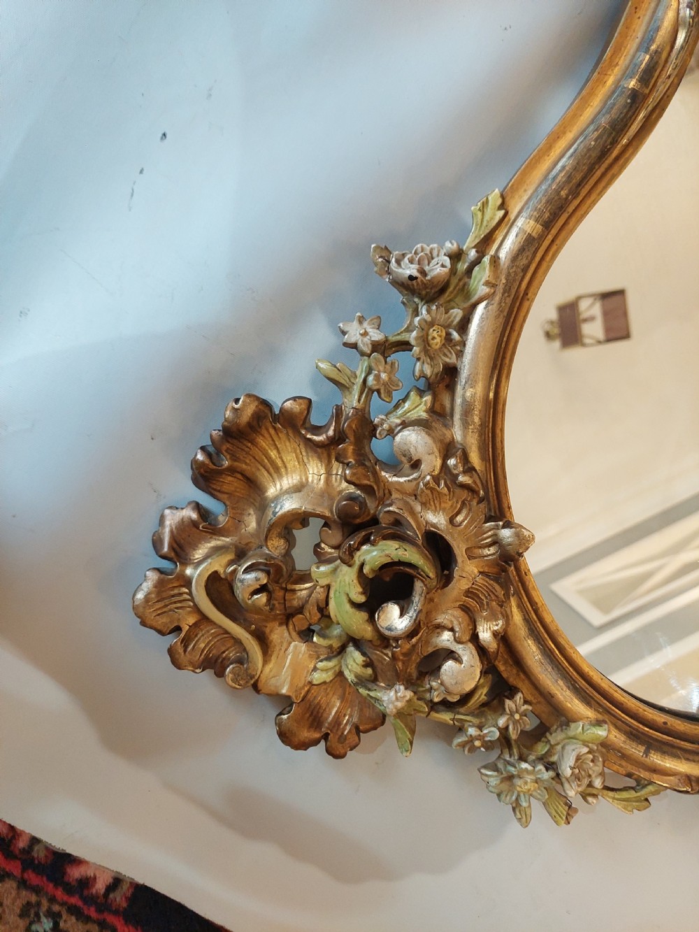 An early 20th-century Italianate giltwood wall mirror featuring an intricate carved crest, asymmetric Rococo scrolls, floral accents, and sculpted putti heads. View V