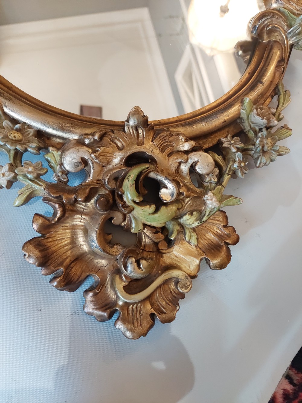 An early 20th-century Italianate giltwood wall mirror featuring an intricate carved crest, asymmetric Rococo scrolls, floral accents, and sculpted putti heads. View VI