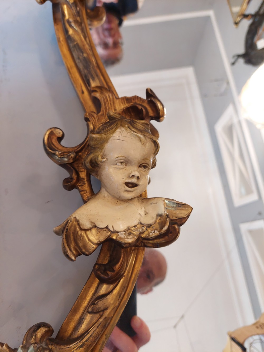An early 20th-century Italianate giltwood wall mirror featuring an intricate carved crest, asymmetric Rococo scrolls, floral accents, and sculpted putti heads. View IX