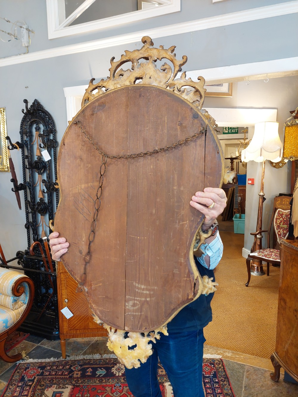 An early 20th-century Italianate giltwood wall mirror featuring an intricate carved crest, asymmetric Rococo scrolls, floral accents, and sculpted putti heads. View X