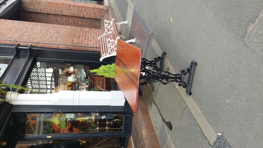 A Victorian style rectangular table featuring a polished timber tabletop supported by black ornate cast iron trestle ends and diagonal bracing. View III