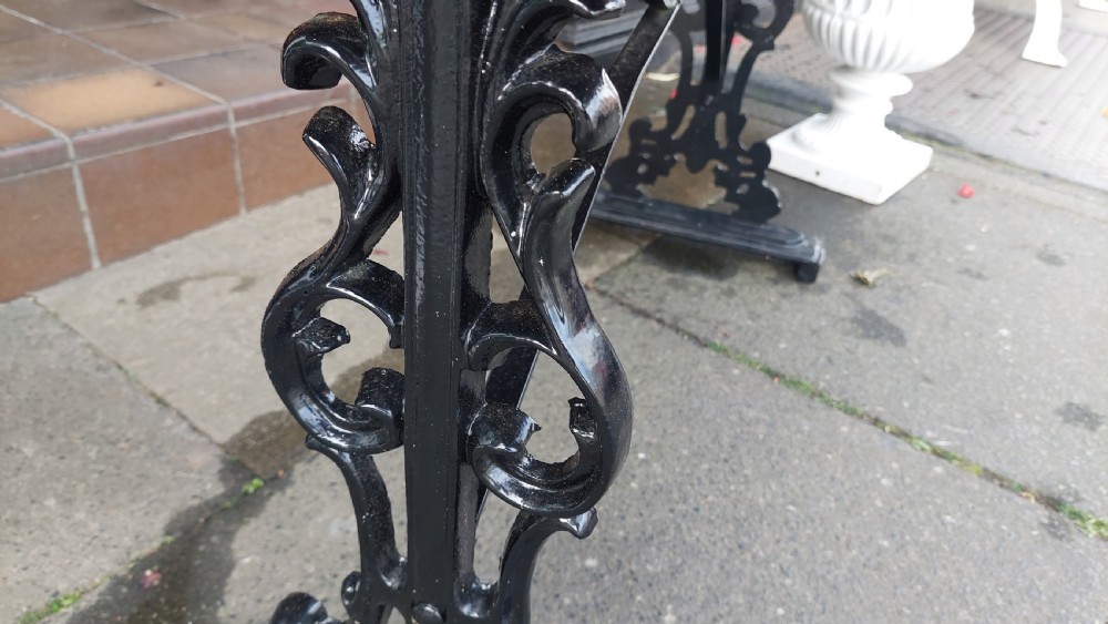 A Victorian style rectangular table featuring a polished timber tabletop supported by black ornate cast iron trestle ends and diagonal bracing. View IV