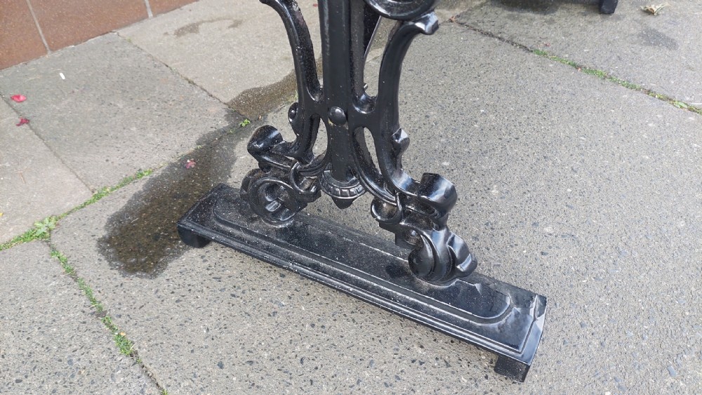 A Victorian style rectangular table featuring a polished timber tabletop supported by black ornate cast iron trestle ends and diagonal bracing. View V