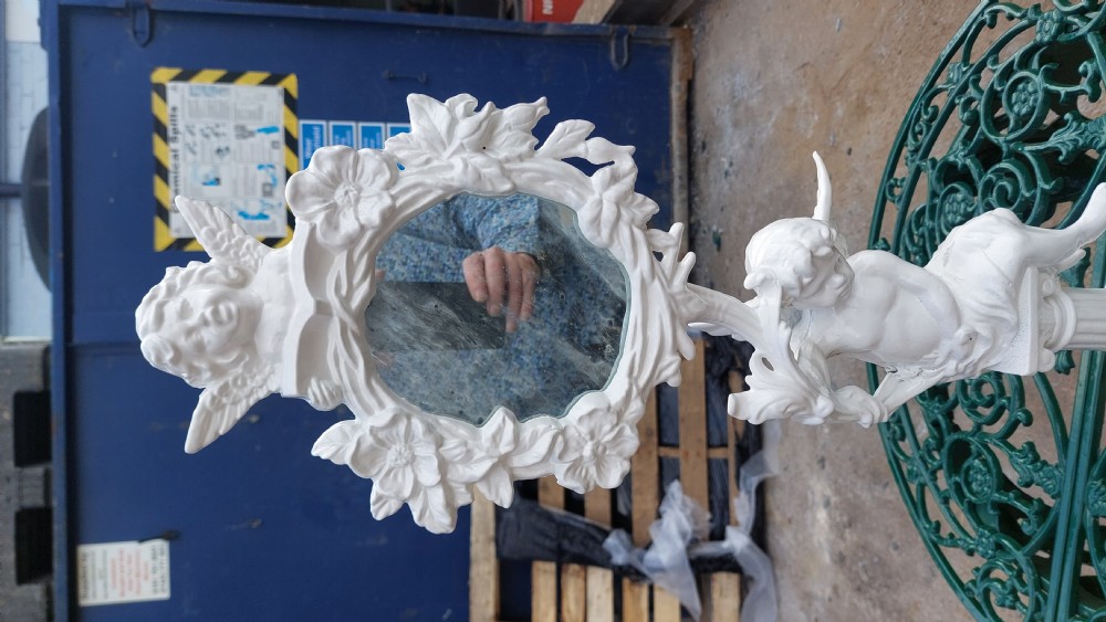 A white-painted cast iron tabletop mirror featuring cherub figures, floral garlands, and a central column pedestal. View IV
