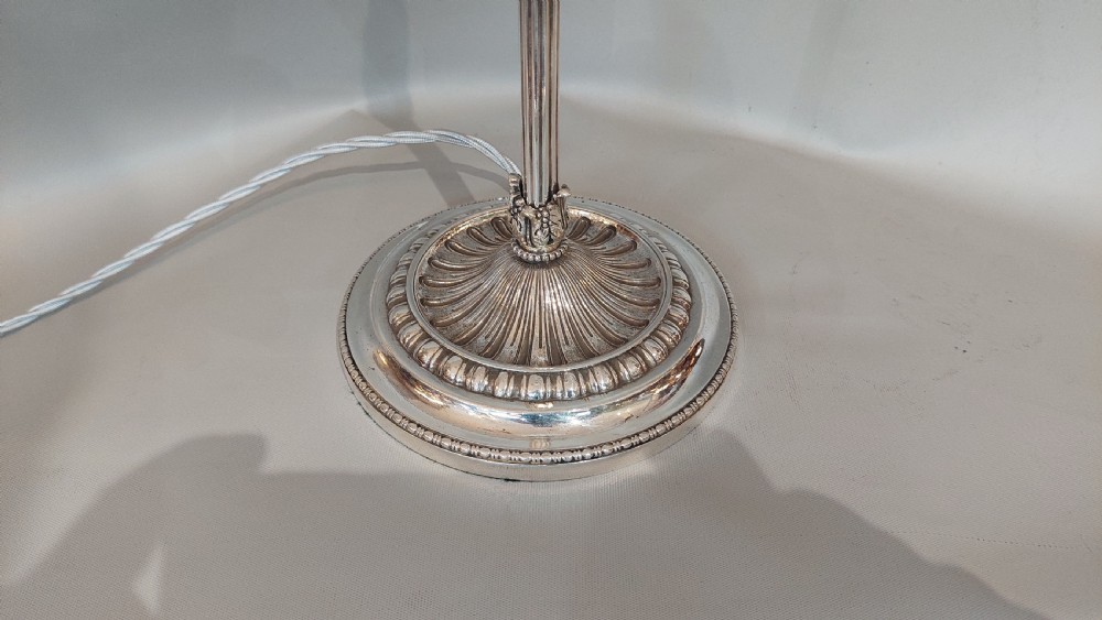An Edwardian silver-plated table lamp featuring a reeded column, circular gadrooned base, pinecone finial, and an oval hoop frame holding a white frilled glass shade. View III