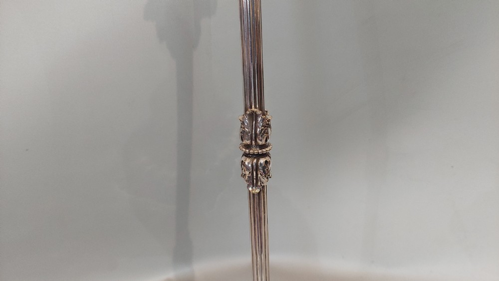 An Edwardian silver-plated table lamp featuring a reeded column, circular gadrooned base, pinecone finial, and an oval hoop frame holding a white frilled glass shade. View IV