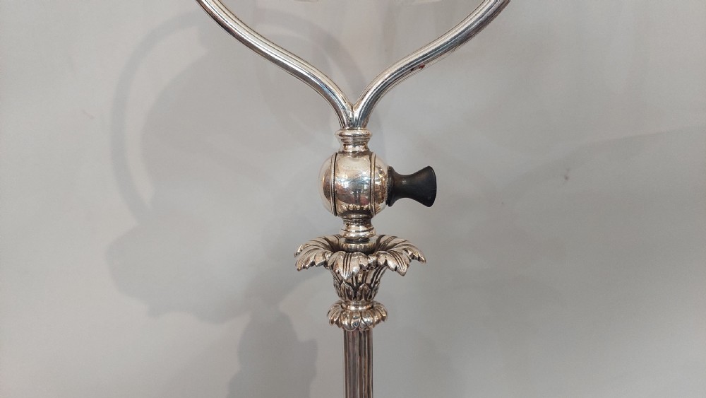 An Edwardian silver-plated table lamp featuring a reeded column, circular gadrooned base, pinecone finial, and an oval hoop frame holding a white frilled glass shade. View V
