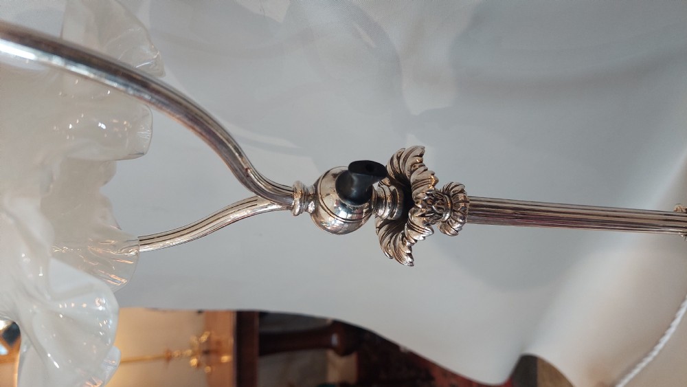 An Edwardian silver-plated table lamp featuring a reeded column, circular gadrooned base, pinecone finial, and an oval hoop frame holding a white frilled glass shade. View VI