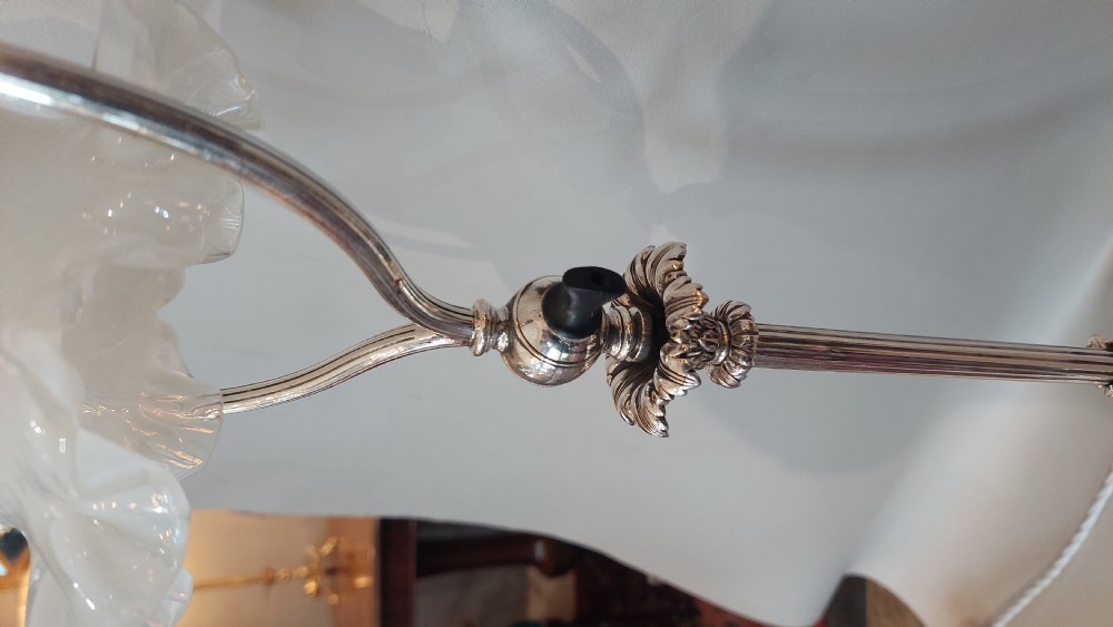 An Edwardian silver-plated table lamp featuring a reeded column, circular gadrooned base, pinecone finial, and an oval hoop frame holding a white frilled glass shade. View VII