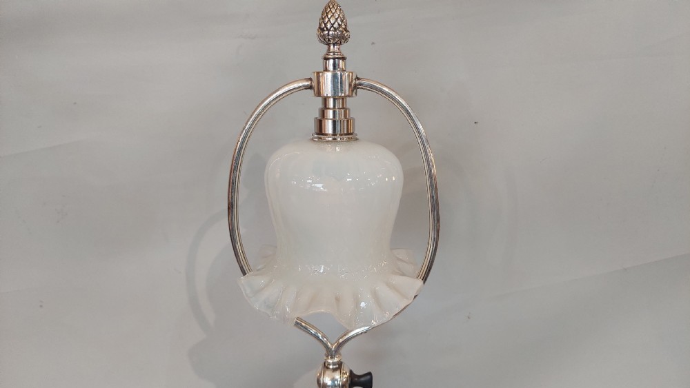 An Edwardian silver-plated table lamp featuring a reeded column, circular gadrooned base, pinecone finial, and an oval hoop frame holding a white frilled glass shade. View VIII
