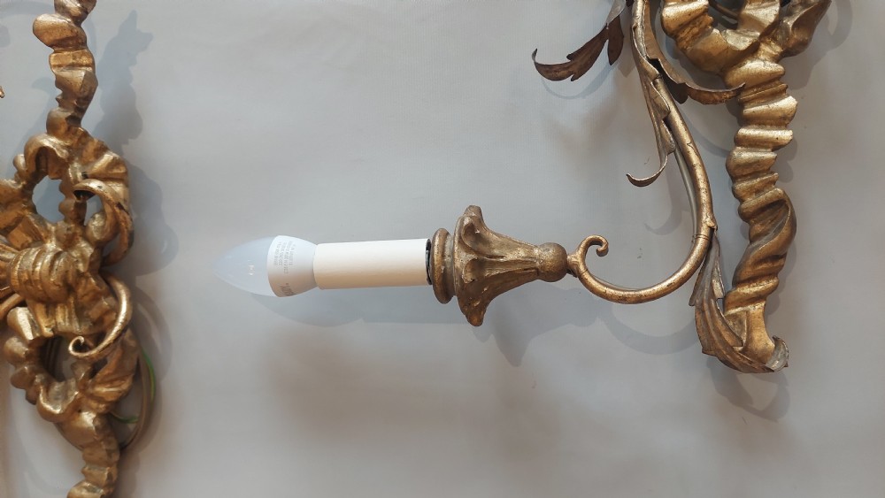 A pair of carved giltwood two-branch wall lights decorated with ribbon bows and foliate leaf scrollwork, holding two candle-style bulbs each. View II