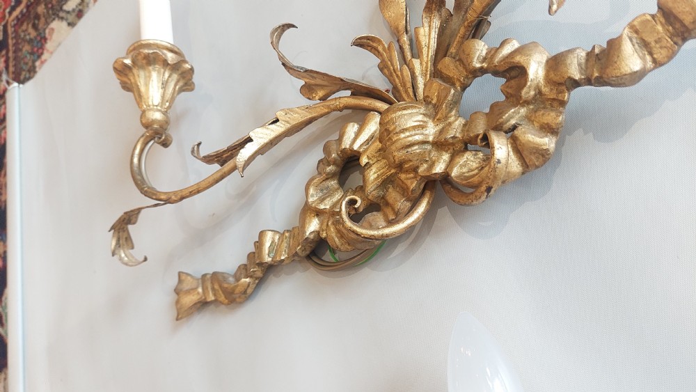 A pair of carved giltwood two-branch wall lights decorated with ribbon bows and foliate leaf scrollwork, holding two candle-style bulbs each. View V