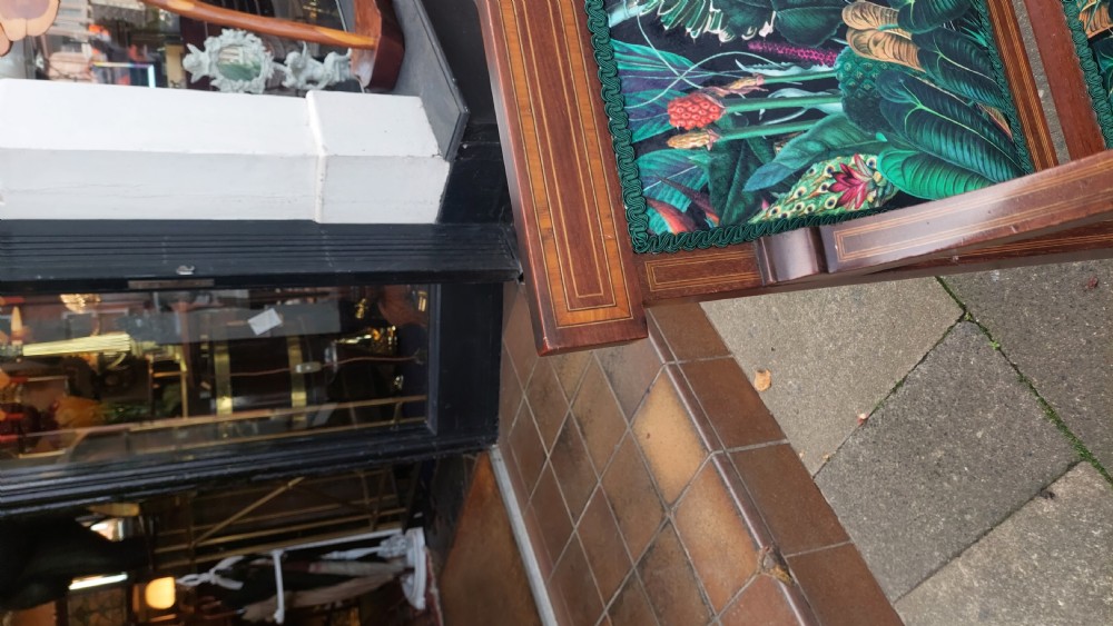An Edwardian inlaid mahogany two-seater settee with swept scroll arms, a central lyre-shaped splat, and green botanical pattern upholstery. View IX