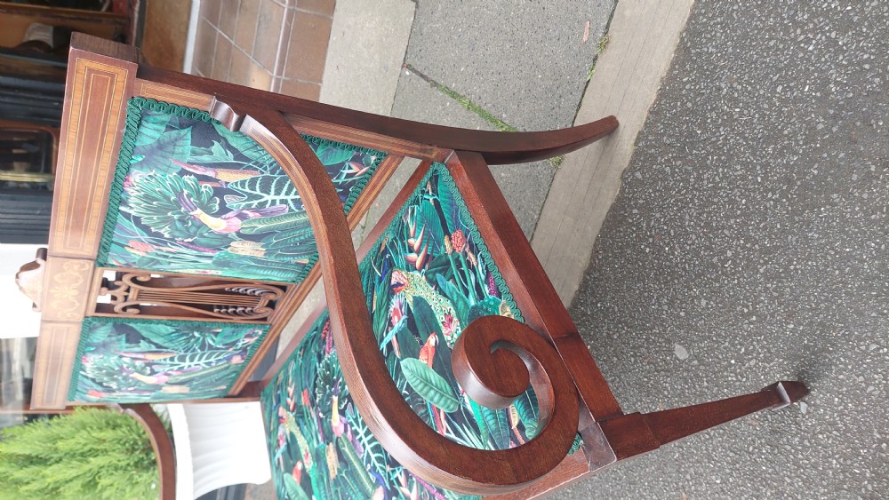 An Edwardian inlaid mahogany two-seater settee with swept scroll arms, a central lyre-shaped splat, and green botanical pattern upholstery. View X