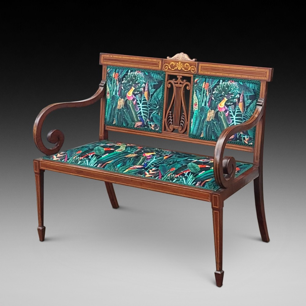 An Edwardian inlaid mahogany two-seater settee with swept scroll arms, a central lyre-shaped splat, and green botanical pattern upholstery.