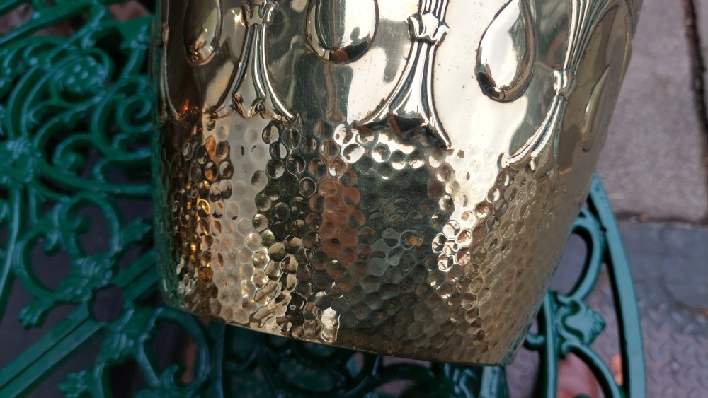 A tapered cylindrical brass planter featuring embossed Art Nouveau floral motifs above a textured hammered base. View VI