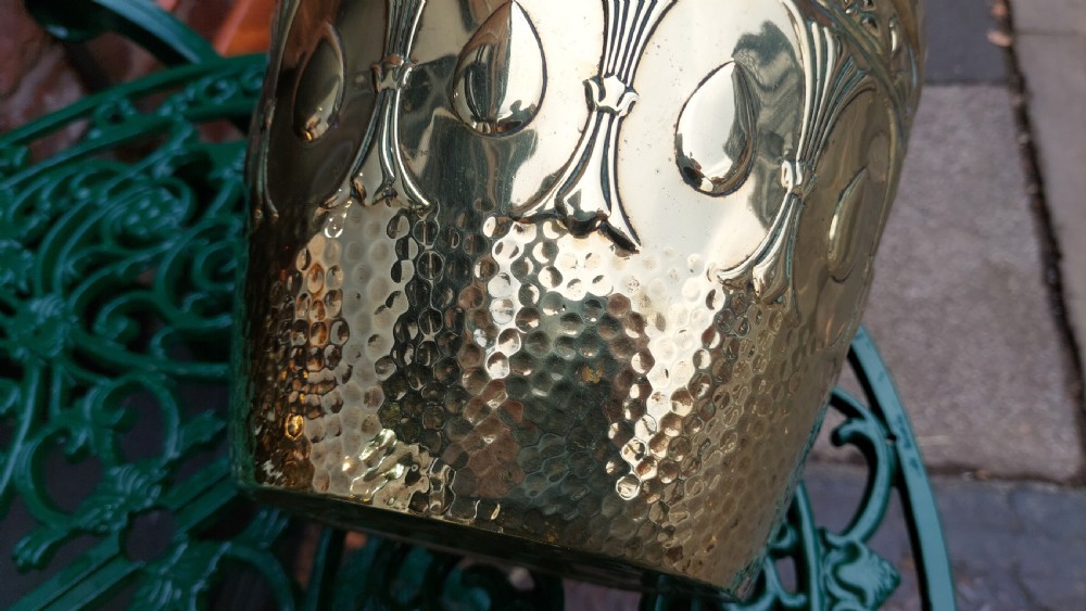 A tapered cylindrical brass planter featuring embossed Art Nouveau floral motifs above a textured hammered base. View VIII