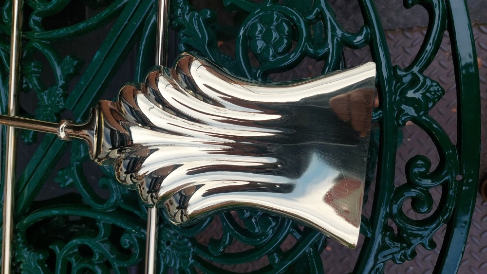 A set of three Victorian polished brass fire irons comprising a poker, a shell-form shovel, and a pair of tongs against a grey gradient background. View III