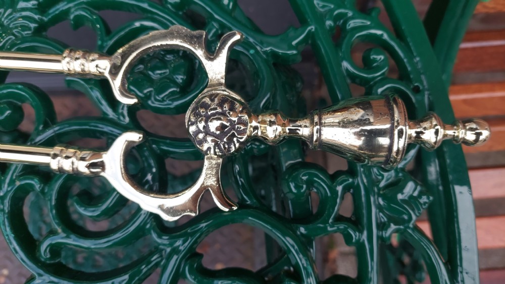 A set of three Victorian polished brass fire irons comprising a poker, a shell-form shovel, and a pair of tongs against a grey gradient background. View VI