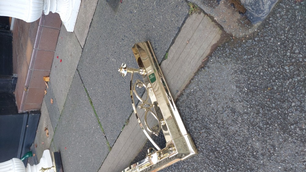 A polished brass extending fireplace fender featuring decorative side gallery rails with scrollwork and urn-shaped corner finials. View IV