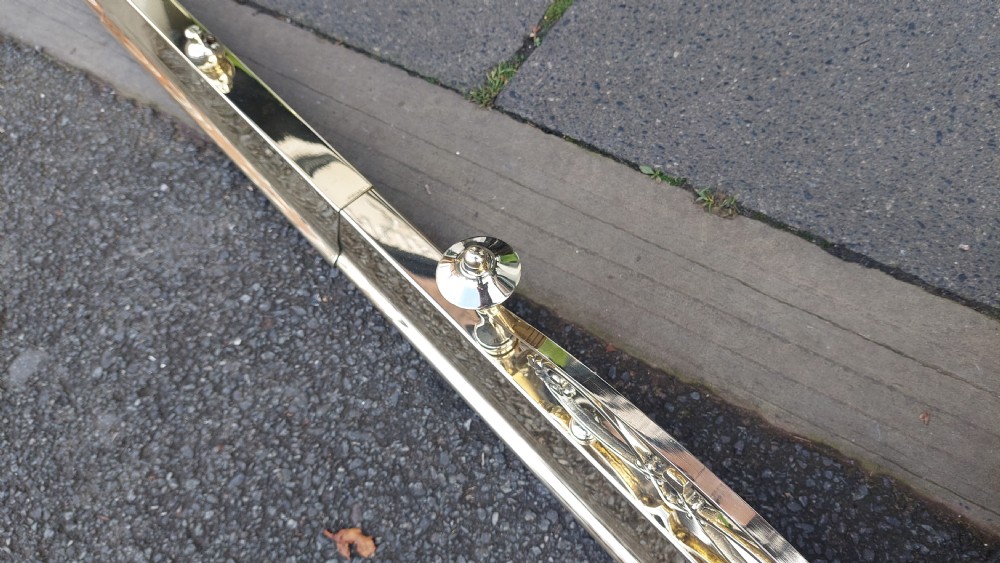 A polished brass extending fireplace fender featuring decorative side gallery rails with scrollwork and urn-shaped corner finials. View VII
