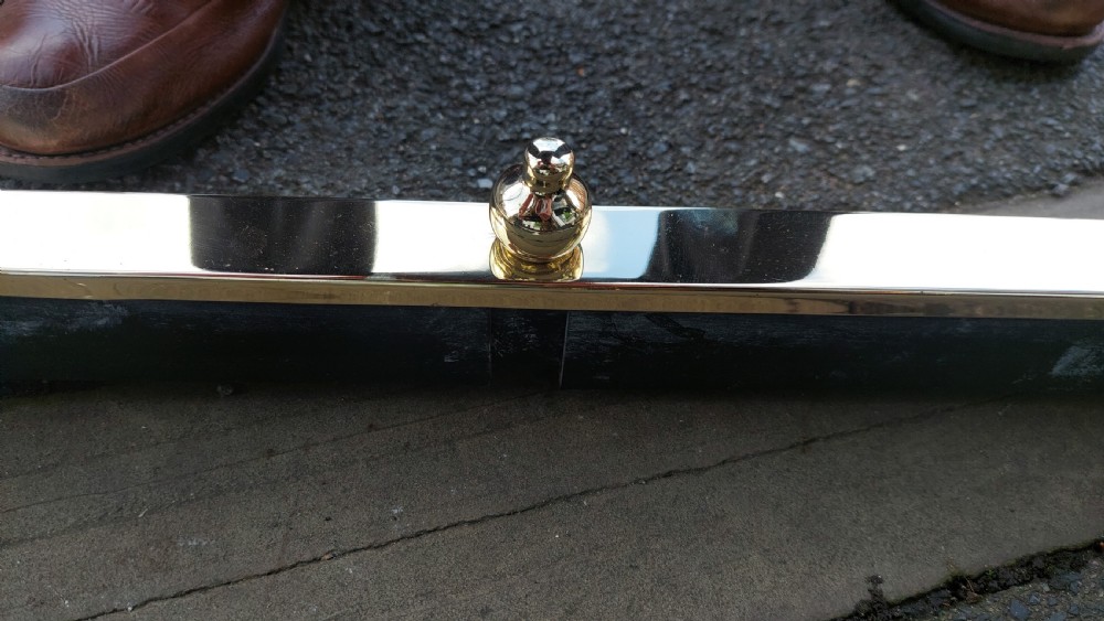 A polished brass extending fireplace fender featuring decorative side gallery rails with scrollwork and urn-shaped corner finials. View X