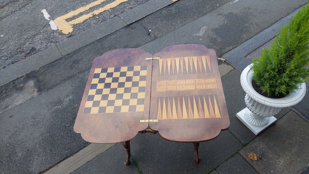 A nineteenth-century burr walnut games and work table featuring marquetry inlay, turned support columns, a lower work well, and carved legs on castors. View V