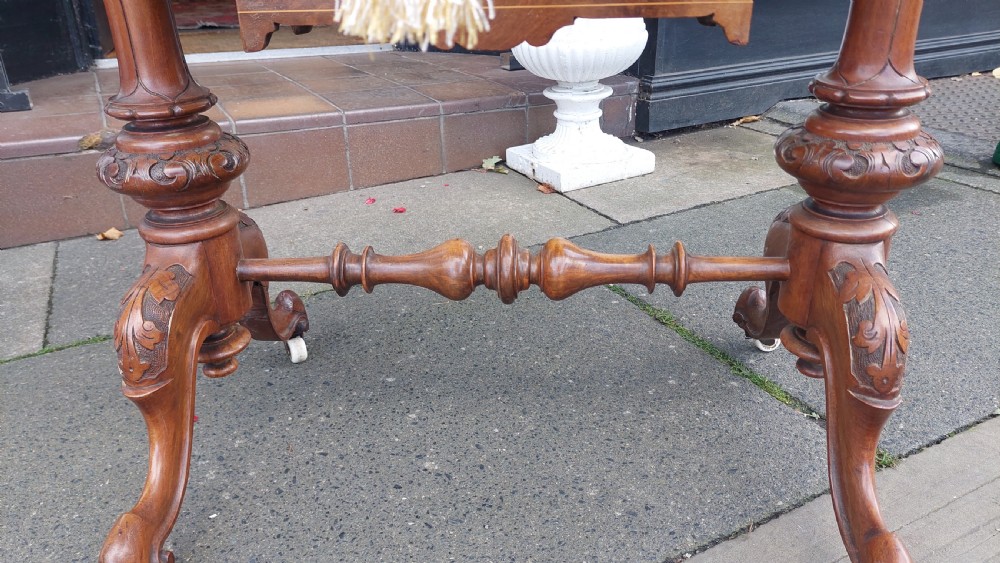 A nineteenth-century burr walnut games and work table featuring marquetry inlay, turned support columns, a lower work well, and carved legs on castors. View X