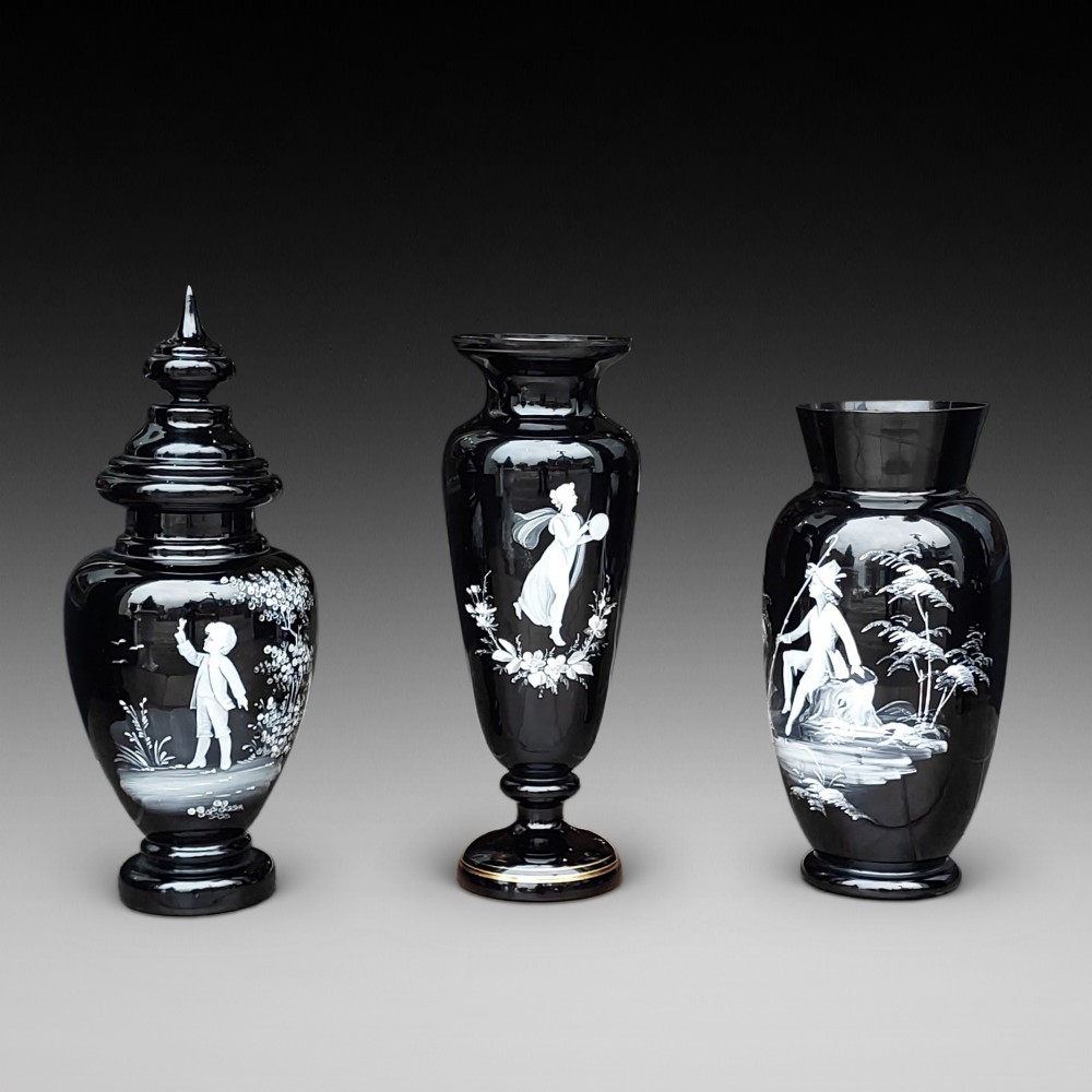 A set of three 19th-century black glass vessels decorated with hand-painted white enamel figures and landscapes.